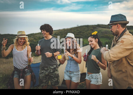 Felice giovani amici di godere di una bella giornata in natura. Si stanno tenendo le bottiglie di birra, ridendo e parlando felici di essere insieme. Foto Stock