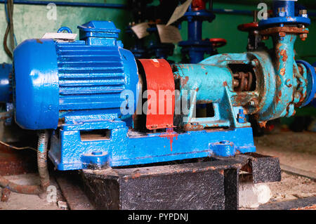 Vecchie e arrugginite graffi pompa acqua con un motore elettrico tinto in colore blu sul tubo dell'acqua fredda. Foto Stock