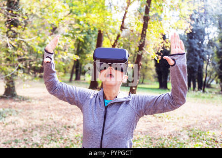 Sorpreso Senior donna divertente con la realtà virtuale auricolare in foresta, VR dispositivo utilizzando le persone anziane. Foto Stock