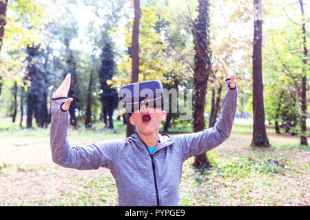 Sorpreso Senior donna divertente con la realtà virtuale auricolare in foresta, VR dispositivo utilizzando le persone anziane. Foto Stock