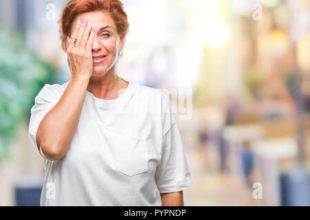 Accattivante senior redhead caucasica donna sullo sfondo isolato che copre un occhio con la mano con fiducioso sorriso sul volto e la sorpresa di emozione. Foto Stock