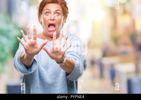 Accattivante senior redhead caucasica donna che indossa un maglione invernale su sfondo isolato paura e il terrore con la paura di espressione gesto di arresto con Foto Stock