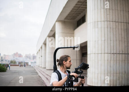 Videografo professionista tenere la fotocamera su 3 assi sospensione cardanica che montato su easy rig. Videografo utilizzando steadicam. Attrezzatura Pro aiuta a rendere i video di alta qualità senza agitazione. Foto Stock