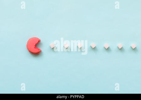 Una composizione di amaretto con una bocca aperta che sta andando a mangiare zollette di zucchero su un pastello blu sullo sfondo. Il concetto di vecchi video giochi. Foto Stock