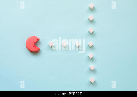 Una composizione di amaretto con una bocca aperta che sta andando a mangiare zollette di zucchero su un pastello blu sullo sfondo. Il concetto di vecchi video giochi. Foto Stock