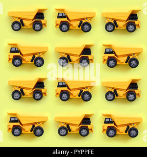 Molti piccoli giallo camion giocattolo su texture di sfondo di moda giallo pastello carta a colori nel concetto di minima. Foto Stock