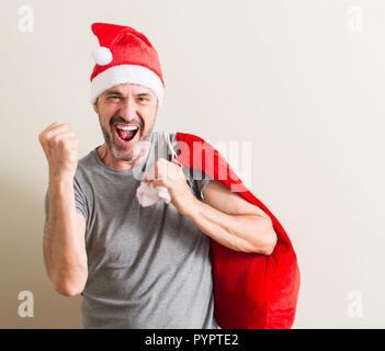 Senior uomo che indossa il natale di santa claus hat urlando orgoglioso e celebrando la vittoria e il successo molto eccitato, allietarla emozione Foto Stock