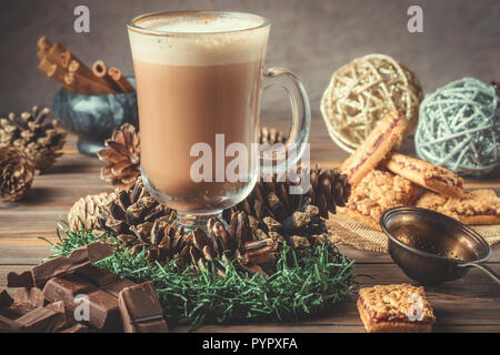 Vetro tazza di cacao o caffè con schiuma di latte sul tavolo di legno serviti biscotti cannella e cioccolato vacanza invernale accessori. Anno nuovo biglietto di auguri di Natale. Foto Stock