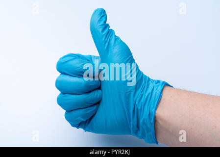 La mano guantata mostra il pollice in su. Il blu guanto medicale al dottore la mano. Foto Stock