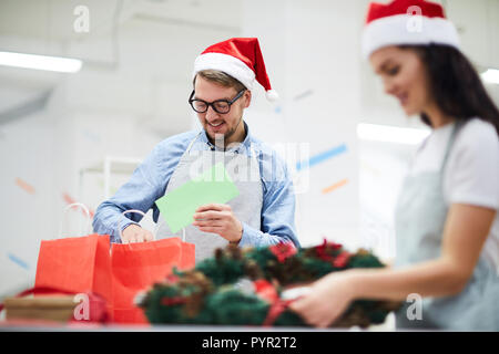 Uomo positivo mettere scheda di Natale nel sacchetto di carta Foto Stock