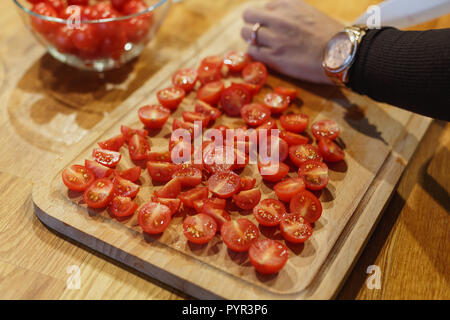 Taglio a mano i pomodori ciliegia sul tagliere di legno il fuoco selettivo Foto Stock
