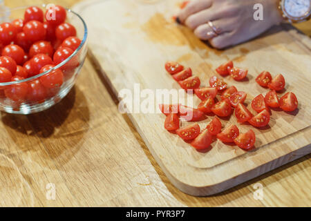 Taglio a mano i pomodori ciliegia sul tagliere di legno il fuoco selettivo Foto Stock
