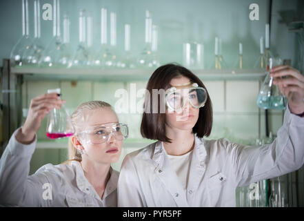 Laboratorio chimico. Due giovani donna tenendo diversi matracci con liquidi in esso Foto Stock