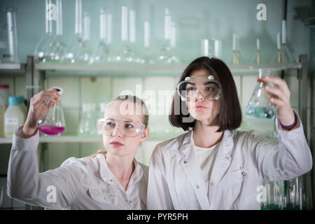 Laboratorio chimico. Due giovani donna tenendo diversi matracci con liquidi in esso. Guardando il pallone Foto Stock