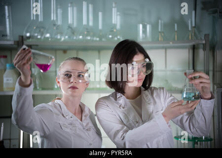 Laboratorio chimico. Due giovani donna in bicchieri di lavoro tenendo diversi matracci con liquidi in esso. Guardando il pallone Foto Stock