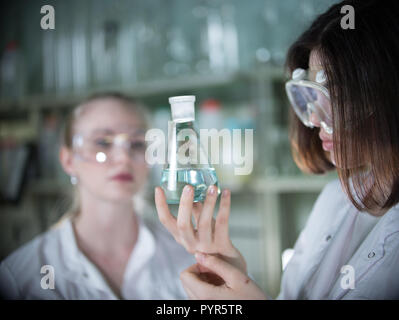 Due giovane donna in laboratorio chimico tenendo un beute con un liquido trasparente in esso Foto Stock