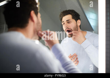 Giovane uomo controllo dente nella stanza da bagno Foto Stock