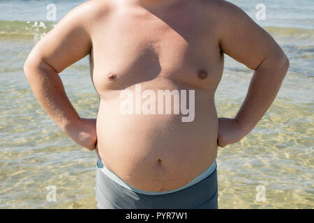 Un uomo grasso in pantaloncini corti sorge sulla riva del mare. Sun e vacanze Foto Stock