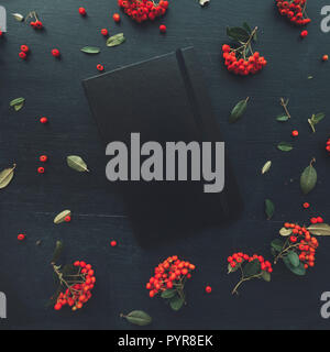 Chiuso moleskin nero notebook laici piatto on dark office desk decorata con frutti di bosco la disposizione di frutta Foto Stock
