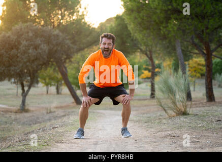 Montare giovane uomo con ginocchio con le sue mani nel dolore dopo aver subito un infortunio muscolare osso rotto dolore alle gambe di distorsione o crampi durante l'esecuzione di un allenamento nel parco Foto Stock