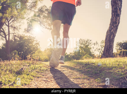 Vista posteriore dello sport uomo con strappato atletico e muscolare di gambe in esecuzione fuori strada in natura in autunno tramonto nella formazione di jogging allenamento in campagna ho Foto Stock