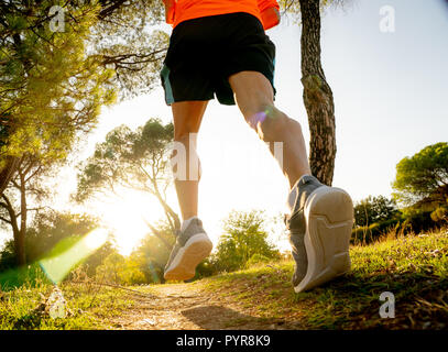 Vista posteriore dello sport uomo con strappato atletico e muscolare di gambe in esecuzione fuori strada in natura in autunno tramonto nella formazione di jogging allenamento in campagna ho Foto Stock