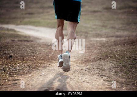 Vista posteriore dello sport uomo con strappato atletico e muscolare di gambe in esecuzione fuori strada in natura in autunno tramonto nella formazione di jogging allenamento in campagna ho Foto Stock