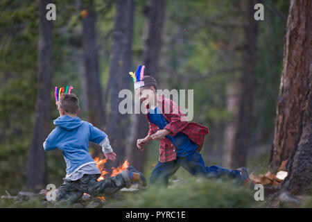 Due giovani fratelli indossando cappelli sfumato mentre si rincorrono in una foresta. Foto Stock