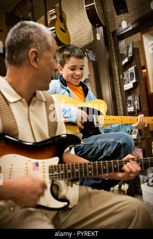 Ragazzo suonando una chitarra elettrica con una metà di uomo adulto in un negozio di musica. Foto Stock