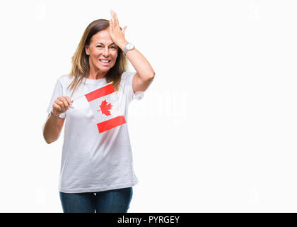 Medioevo donna ispanica holding bandiera del Canada su sfondo isolato ha sottolineato con la mano sulla testa, sconvolto con vergogna e la sorpresa di fronte, e arrabbiato Foto Stock