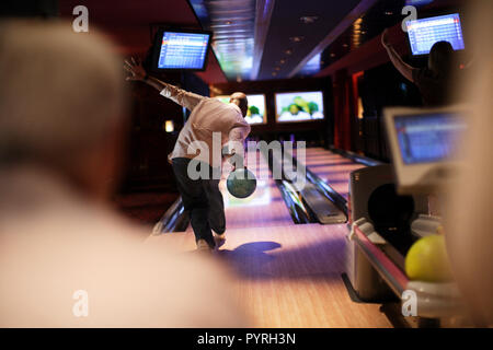 Metà uomo adulto bowling una sfera su una pista da bowling guardato su da amici. Foto Stock