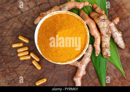 La curcuma in polvere in ciotole di legno e la curcuma capsule su sfondo di legno Foto Stock