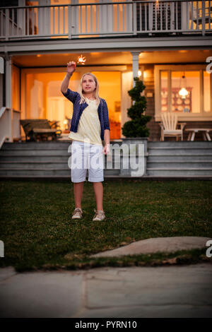 Giovane ragazza che gioca con un sparkler nel suo cortile. Foto Stock