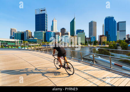 Un uomo in bicicletta su Elizabeth Quay ponte con una vista della città di Perth in background. Elizabeth Quay Foto Stock