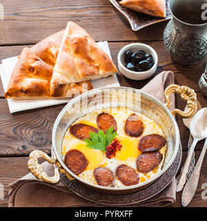 Bagno turco colazione - uova fritte con salsicce (sucuk) e spezie in un tegame su un sfondo di legno. Foto Stock