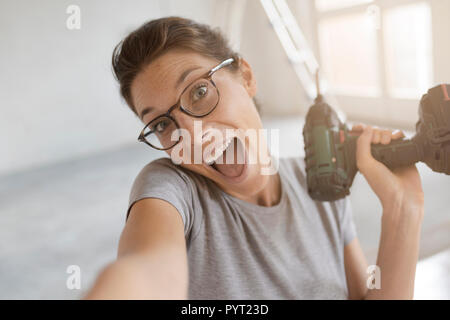 Felice Allegra donna tenendo un trapano e prendendo un selfie, home rinnovo e Do it yourself concept Foto Stock