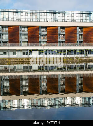 Moderno blocco di appartamenti sul lungofiume, Riva, Leith, Edimburgo, Scozia, Regno Unito simmetrica con la riflessione in acqua di Leith fiume sulla giornata di sole Foto Stock