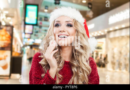 Donna felice in Santa hat divertirsi su shopping mall dello sfondo. Natale o Capodanno vendita e offrire nozione Foto Stock