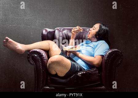 Asian fat man snacking ciambelle sul lettino a casa Foto Stock