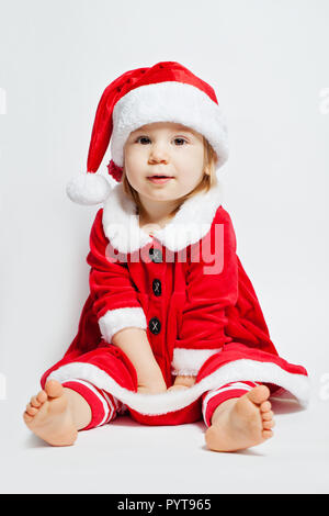 Natale bambino ragazza in Santa hat seduto su sfondo bianco Foto Stock