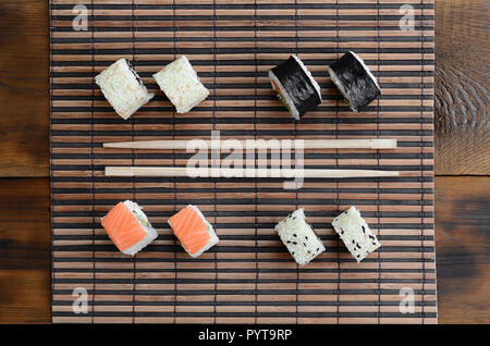 Rotoli di Sushi e bacchette di legno giacciono su una cannuccia di bambù serwing mat. Tradizionale cibo asiatico. Vista dall'alto. Foto Stock