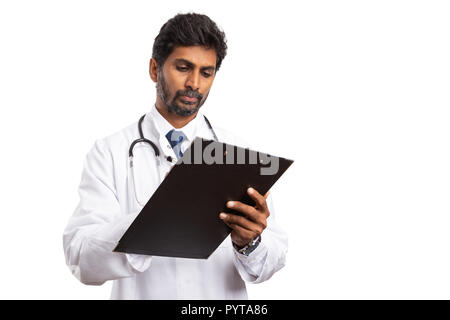 Medico indiano maschio in cerca focalizzata e prendere appunti su appunti con penna isolati su sfondo bianco Foto Stock