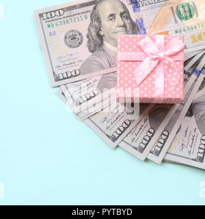 Rosa punteggiato confezione regalo si trova nei pressi di centinaia di dollari su un fondo azzurro. Foto Stock