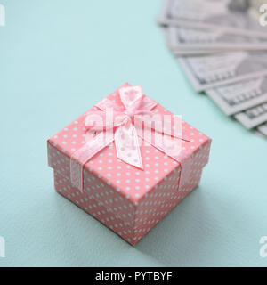 Rosa punteggiato confezione regalo si trova nei pressi di centinaia di dollari su un fondo azzurro. Foto Stock