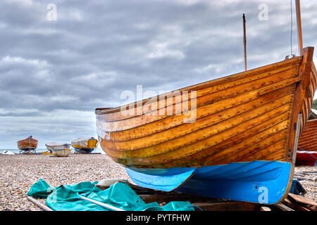 Spiaggiata imbarcazione in legno sulla spiaggia di birra nel Devon, in Inghilterra con spiaggiata barche in background e moody cielo molto nuvoloso Foto Stock