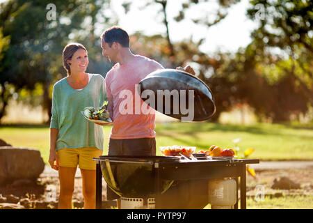 Coppia sorridente cottura su un barbecue nel loro back yard. Foto Stock