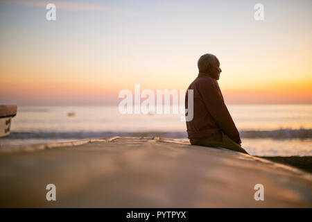 Malinconici uomo maturo seduto su una spiaggia al tramonto. Foto Stock