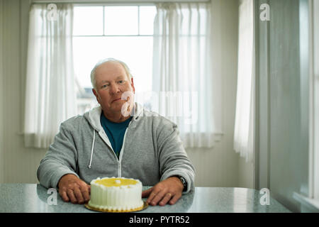 Ritratto di un anziano uomo seduto di fronte a una torta di compleanno. Foto Stock