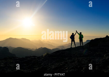 Giovane escursionisti per celebrare il successo nel tramonto montagne, ottenere con le braccia in alto proteso. Giovane uomo e donna che guarda alla splendida ispirazione la Foto Stock