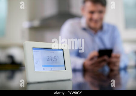 L'uomo il controllo di riscaldamento centrale Smart Meter utilizzando App sul telefono cellulare Foto Stock